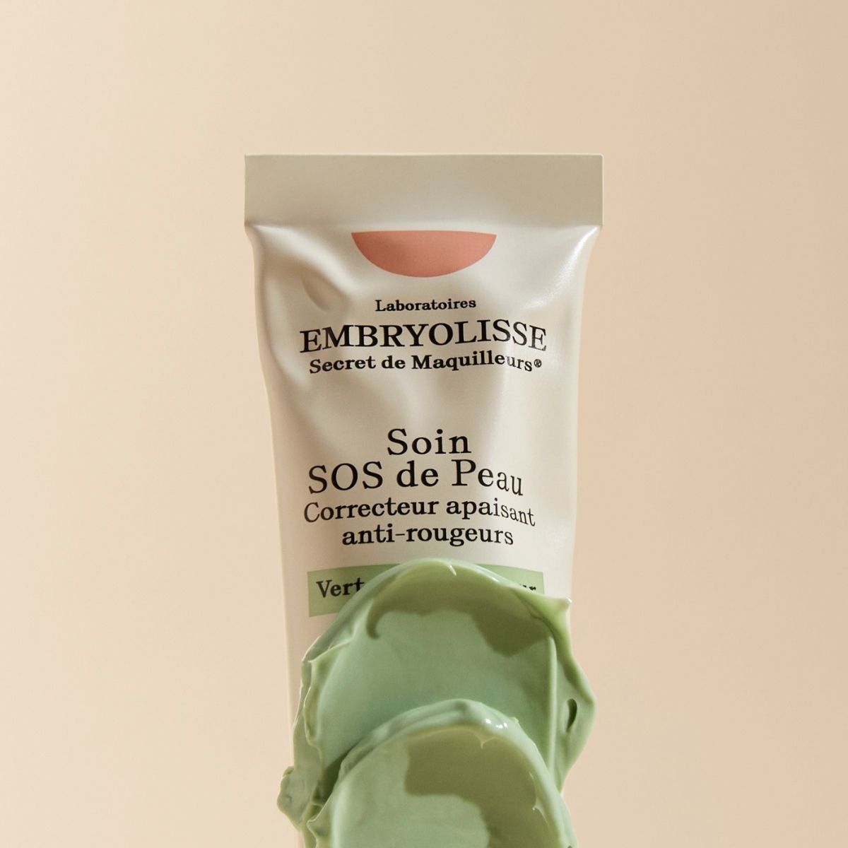 Embryolisse skincare SOS Corrective Cream anti-redness green neutralizer in a beige tube, shown with a thick swirl of light green cream in the foreground, highlighting the soothing corrective texture for sensitive and redness-prone skin.