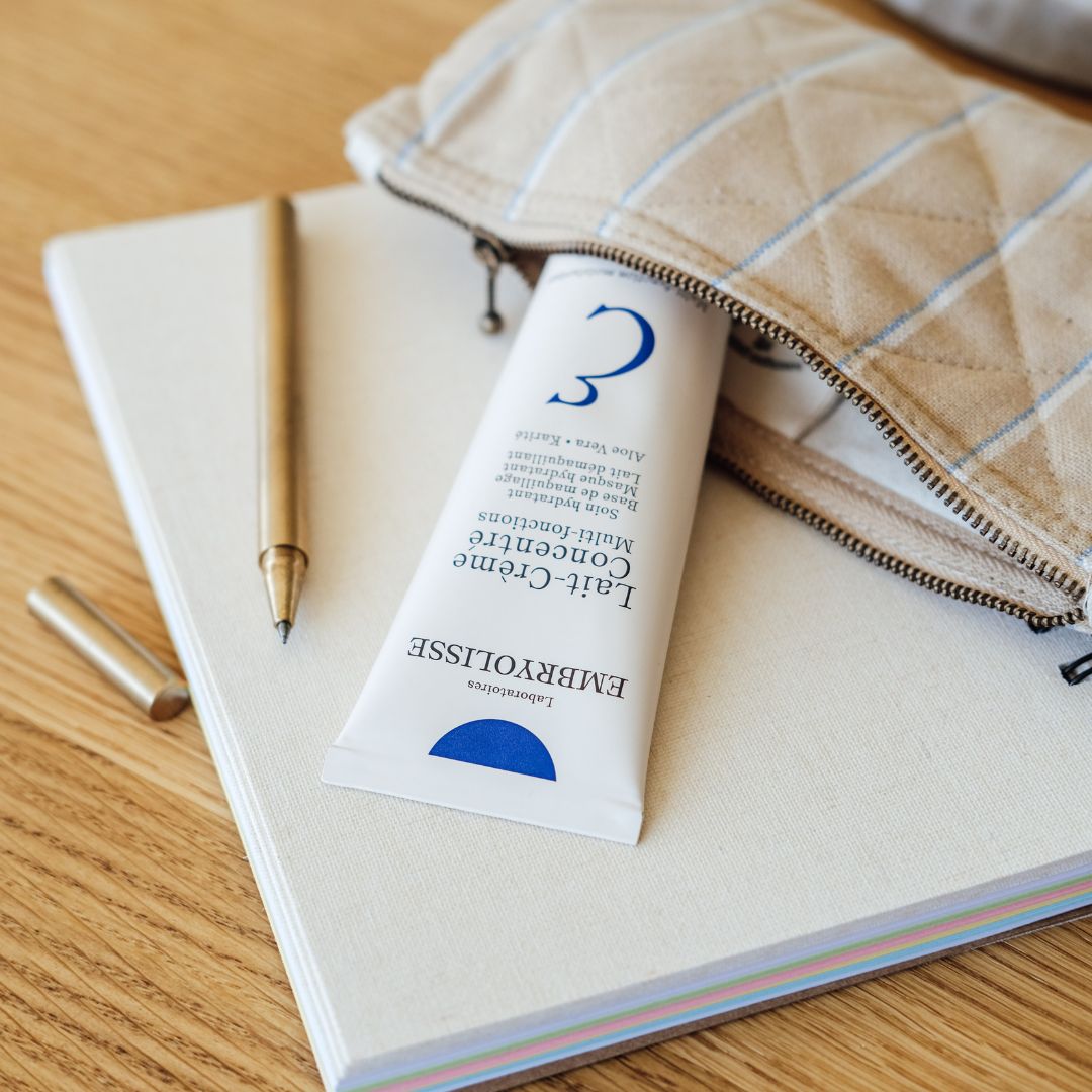 Tube of multifunction Lait-Crème Concentré by Embryolisse skincare on a notebook with a pen and pouch in the background.