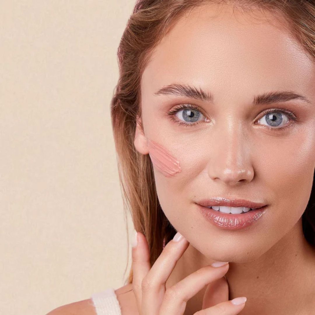 Woman with Radiant Complexion Cream - Pink Glow skincare product by Embryolisse on her face against a beige background