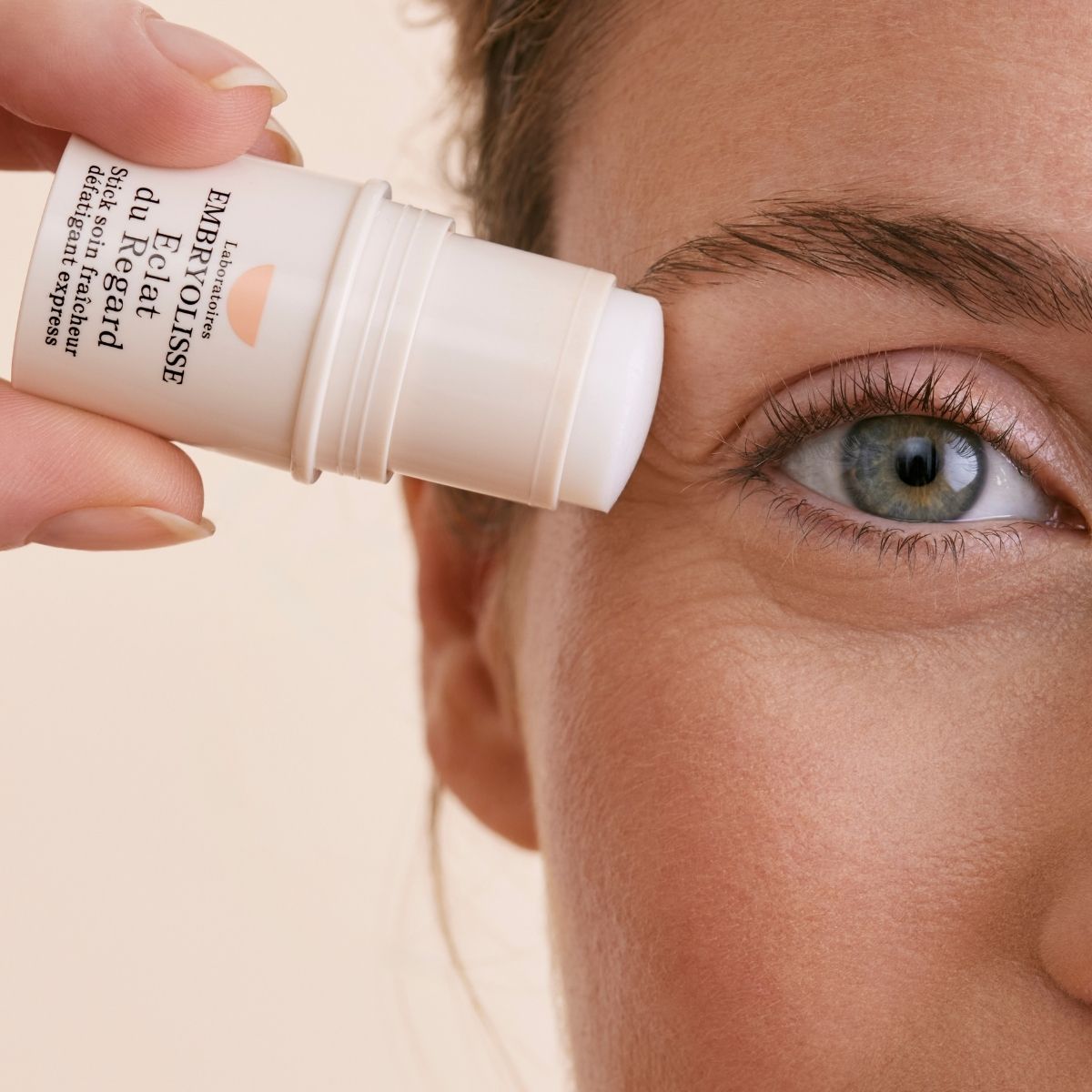 A person applying the Radiant Eye Stick to their eye area with a beige background