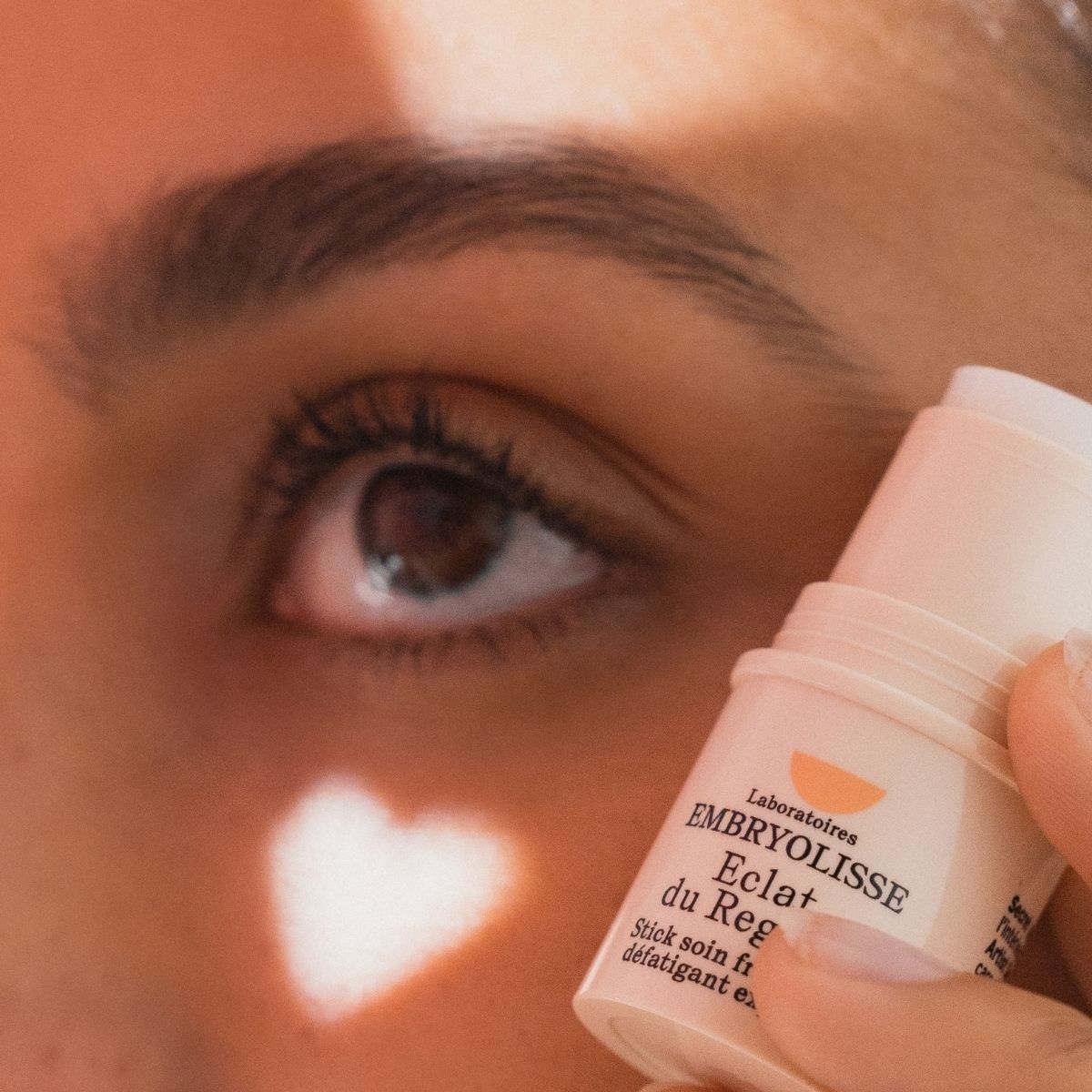 Person showing Embryolisse Radiant Eye Stick eye contour care to their eye area with a heart-shaped light effect.