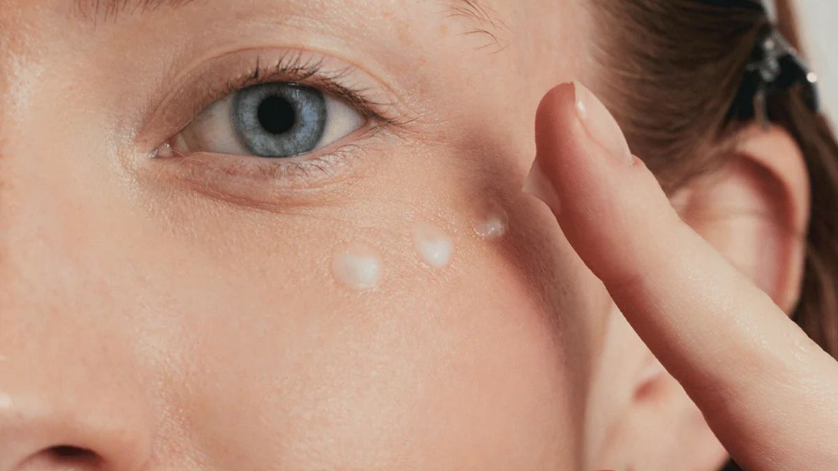 Closeup of a women eye and her under eye are. She's applying peas of eye contour cream by Embryolisse