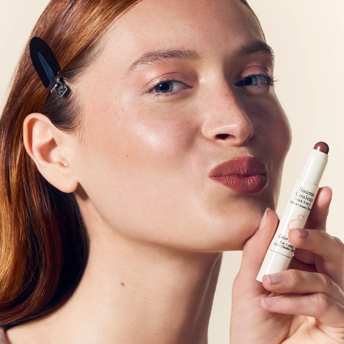 Model wearing Embryolisse Artist Secret Color Balm 3-in-1 Stick Mocha on lips and cheeks