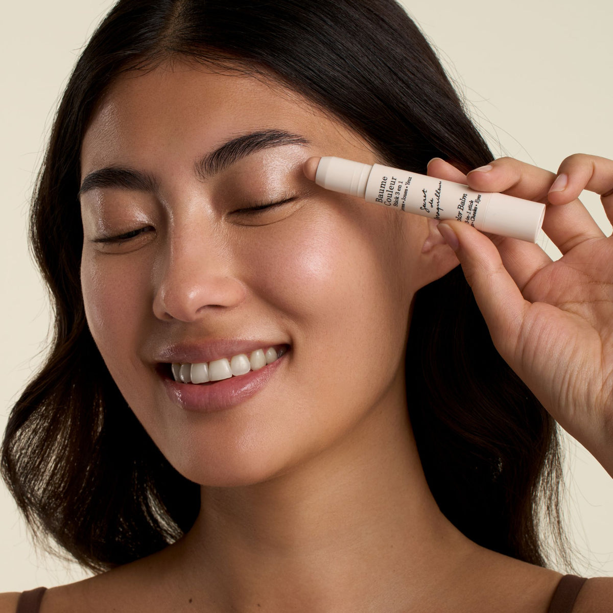 Smiling model sweeping the Color Balm 3-in-1 Stick in Champagne across the eyelid as a shimmering cream eyeshadow
