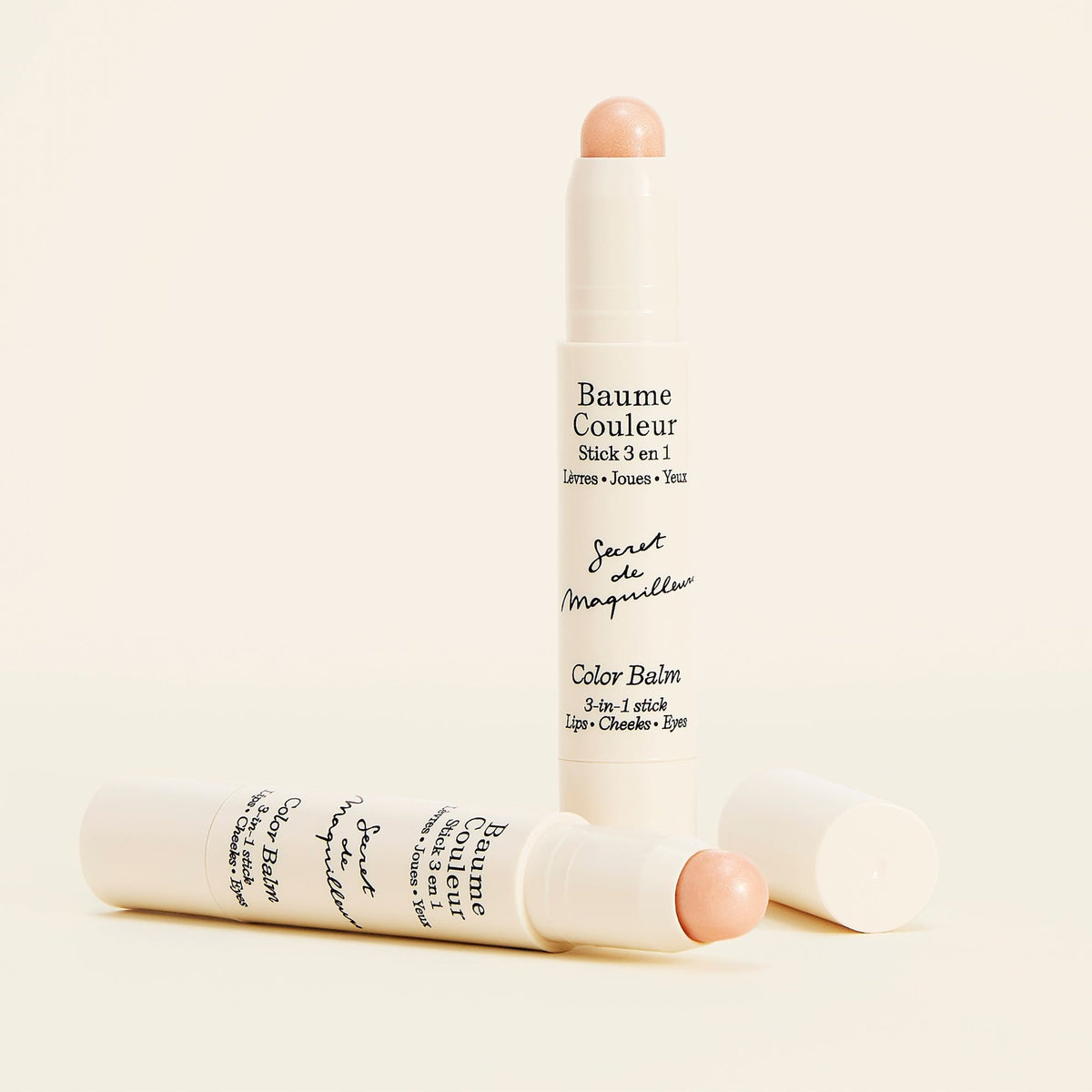 Two Color Balm 3-in-1 Sticks in Champagne, one standing and one lying beside its cap, showing the light-reflecting shade