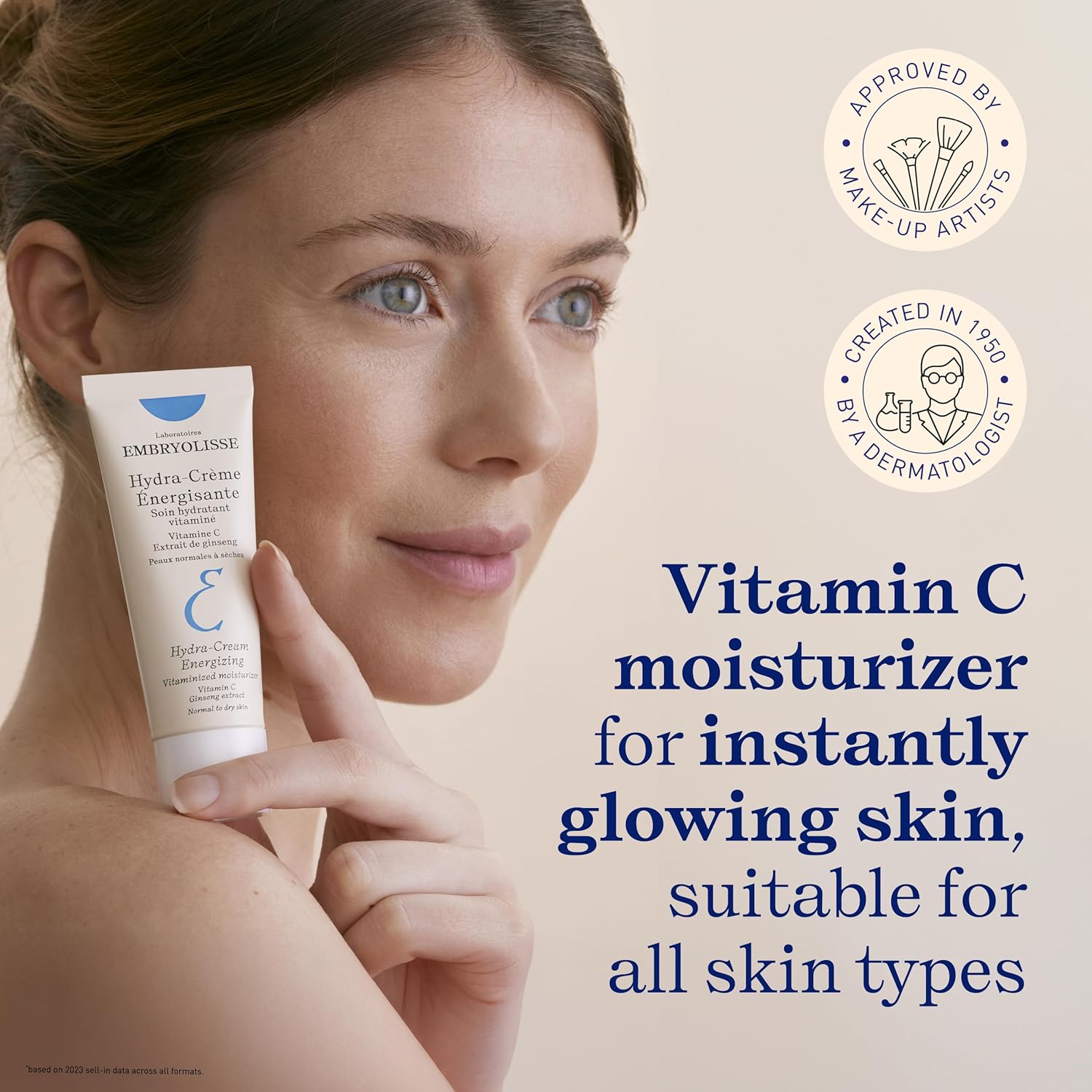 Woman holding a Hydra-Creasm energizing skincare by Embryolisse with text about Vitamin C moisturizer on a beige background