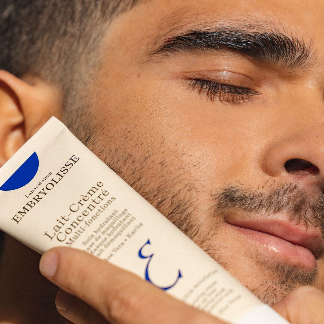 A man holding Embryolisse Lait-Crème Concentré skincare product close to his face