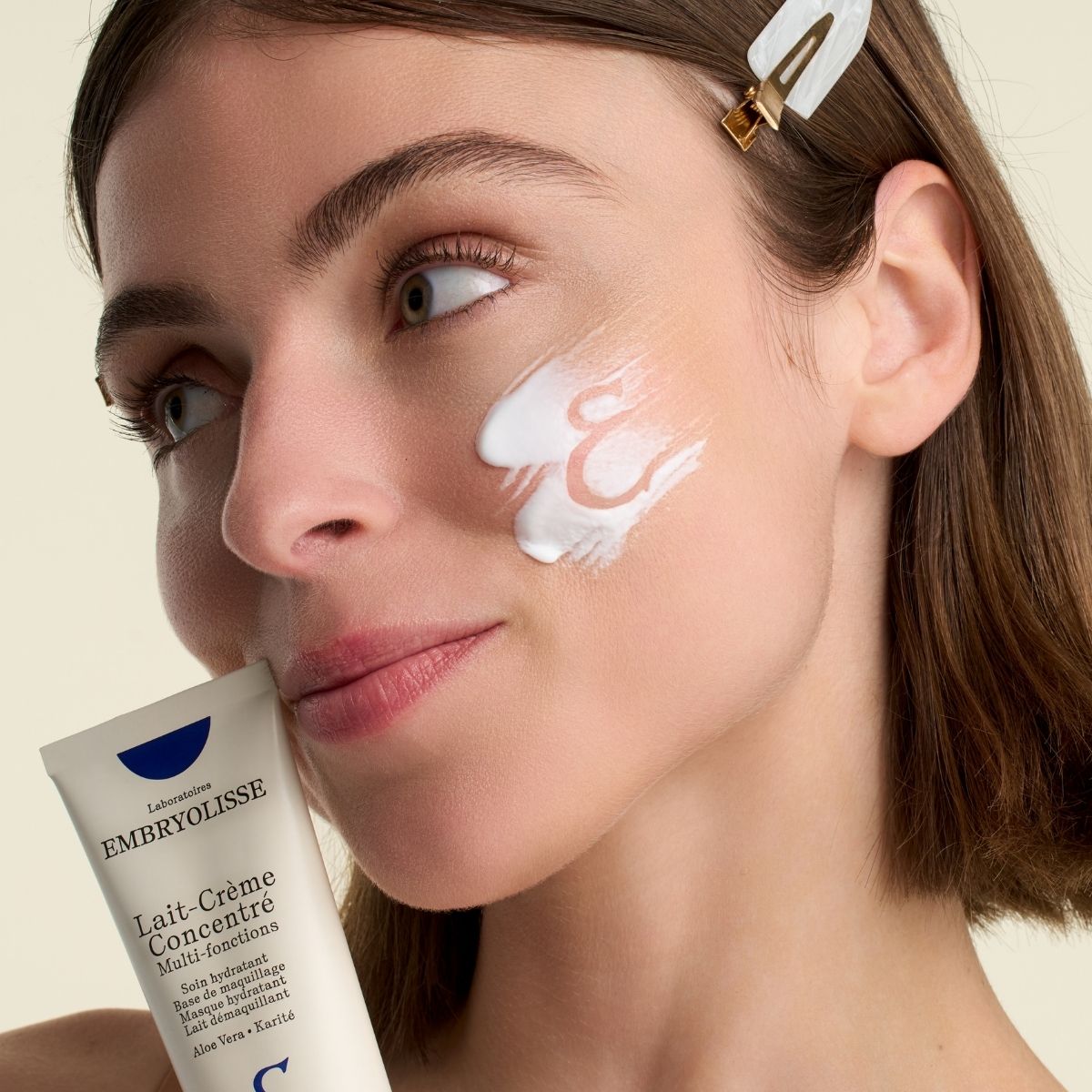 Woman showing a tube of Embryolisse Lait-Crème Concentré bestseller and texture of the moisturizer on he face