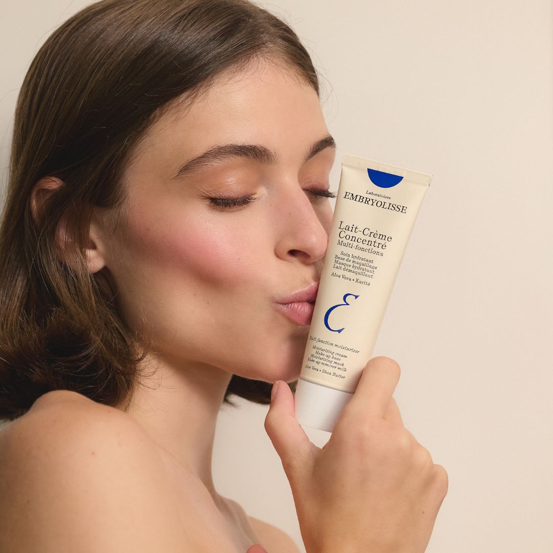 Woman kissing a tube of Embryolisse Lait-Crème Concentré against a neutral background