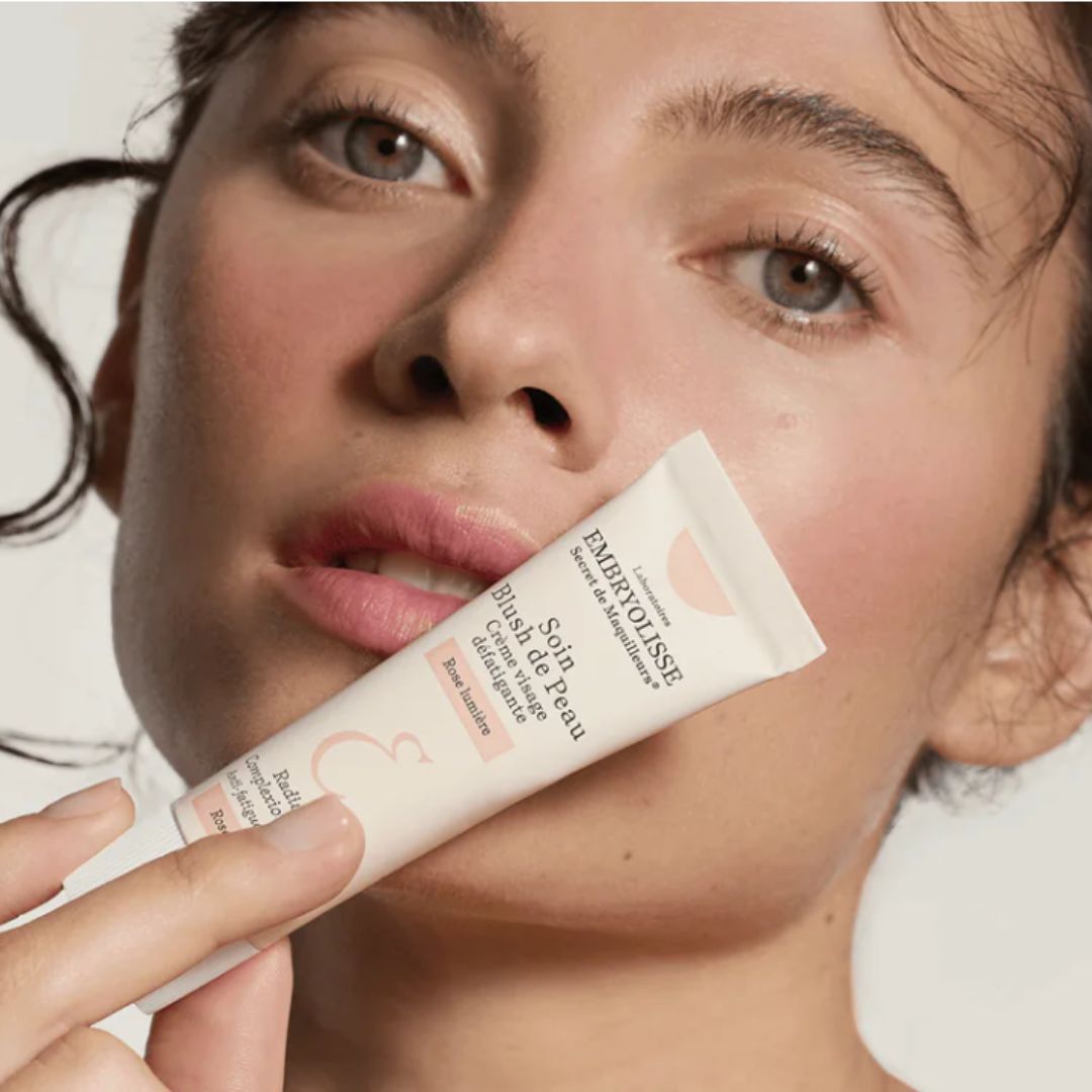 Woman holding the Radiant Complexion Cream - Pink Glow skincare product by Embryolisse close to her face